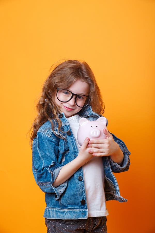 Gelukkig meisje in yeglasses met een spaarvarken op oranje achtergrond royalty-vrije stock fotografie Gelukkig meisje in yeglasses met een spaarvarken op oranje achtergrond royalty-vrije stock fotografie