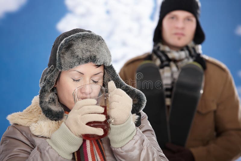 Young couple in snow at winter wearing warm clothes, smiling. Woman drinking cup of hot tea. Young couple in snow at winter wearing warm clothes, smiling. Woman drinking cup of hot tea.