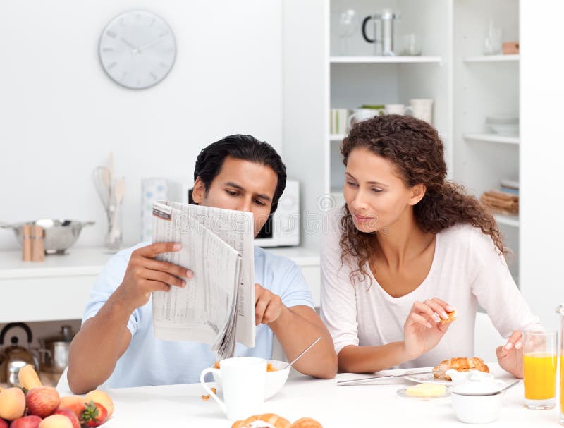 Happy couple reading the newspaper at breakfast in the kitchen. Happy couple reading the newspaper at breakfast in the kitchen