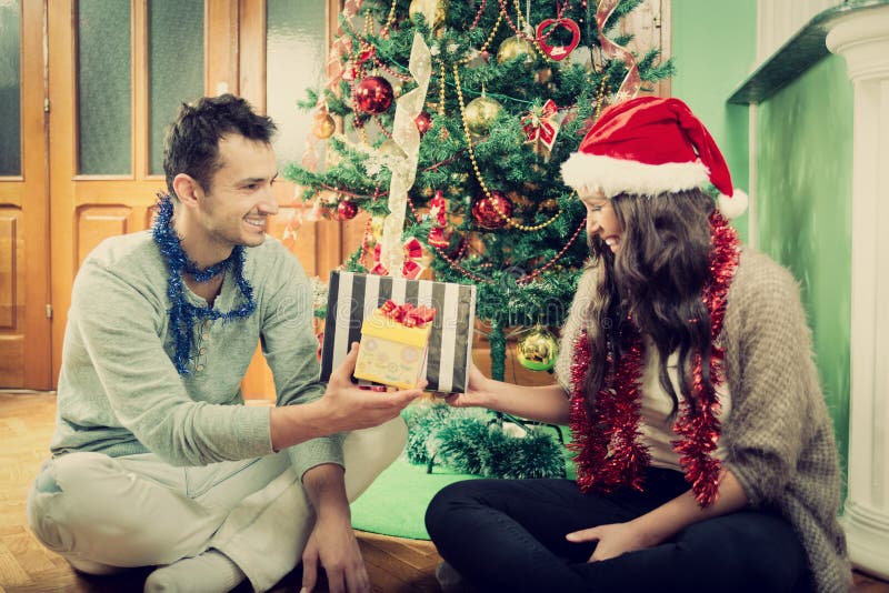Gelukkig paar die giften ruilen thuis door Kerstboom royalty-vrije stock fotografie Gelukkig paar die giften ruilen thuis door Kerstboom royalty-vrije stock fotografie