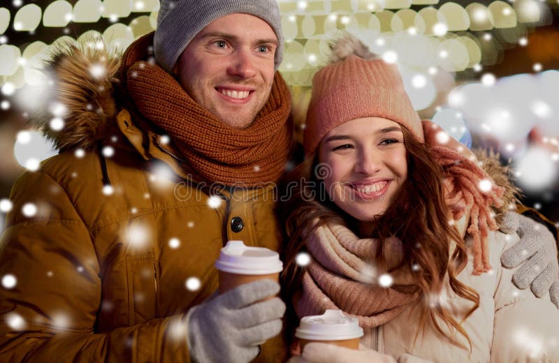 Winter holidays, hot drinks and people concept - happy young couple with coffee over christmas lights in evening. Winter holidays, hot drinks and people concept - happy young couple with coffee over christmas lights in evening