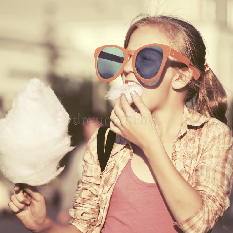 Gelukkig tienermeisje die in zonnebril gesponnen suiker in stadsstraat eten stock fotografie Gelukkig tienermeisje die in zonnebril gesponnen suiker in stadsstraat eten stock fotografie