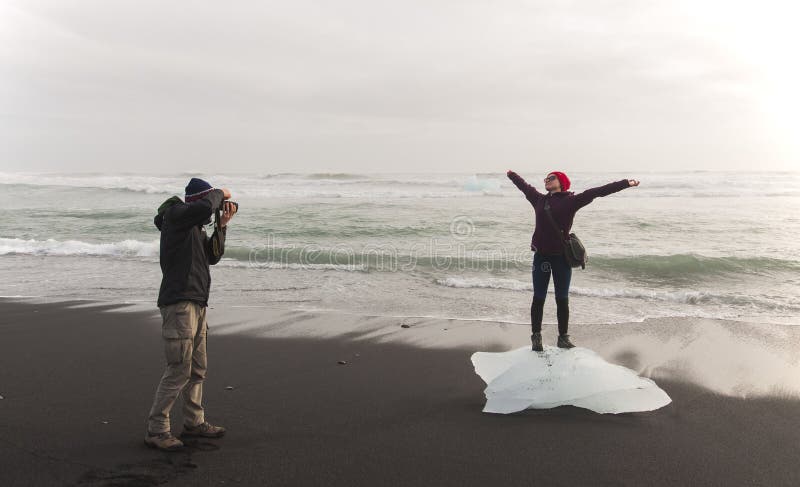 Gelukkig toeristenpaar die een foto op het zwarte strand IJsland nemen stock afbeelding Gelukkig toeristenpaar die een foto op het zwarte strand IJsland nemen stock afbeelding