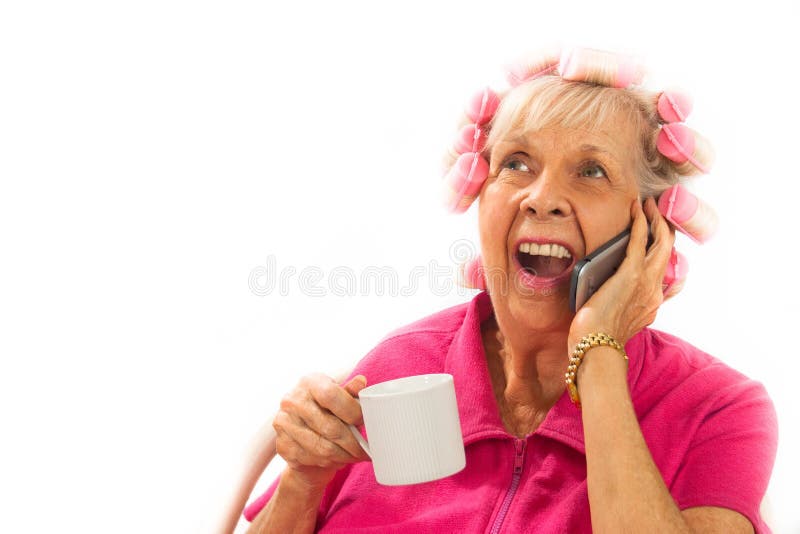 A happy, surprised expression lights up the face of a senior lady in curlers who listens to her cell phone while she holds a coffee cup. A happy, surprised expression lights up the face of a senior lady in curlers who listens to her cell phone while she holds a coffee cup.