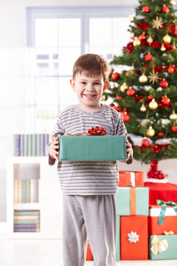 Happy little boy standing with christmas present in hand in morning light, smiling at camera. Happy little boy standing with christmas present in hand in morning light, smiling at camera.