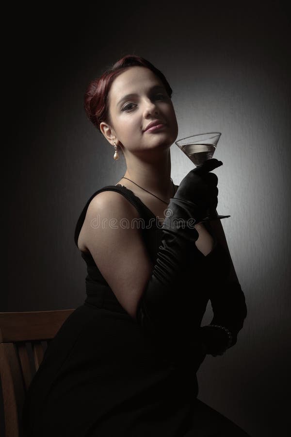 Gelukkige aantrekkelijke vrouw in zwarte kleding met perfect haar en make-upholdingsglas van martini stock afbeelding Gelukkige aantrekkelijke vrouw in zwarte kleding met perfect haar en make-upholdingsglas van martini stock afbeelding