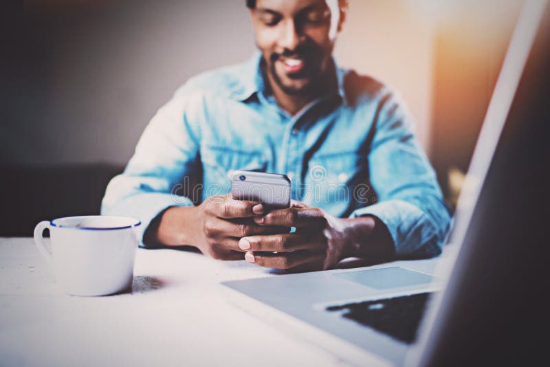 Gelukkige Afrikaanse mens die smartphone gebruiken terwijl het zitten van bij de houten lijst zijn modern huis Concept jongeren h royalty-vrije stock foto Gelukkige Afrikaanse mens die smartphone gebruiken terwijl het zitten van bij de houten lijst zijn modern huis Concept jongeren h royalty-vrije stock foto