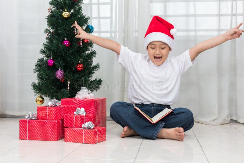 Gelukkige Aziatische Chinees weinig boek van de jongenslezing naast Kerstmis pre stock afbeelding Gelukkige Aziatische Chinees weinig boek van de jongenslezing naast Kerstmis pre stock afbeelding