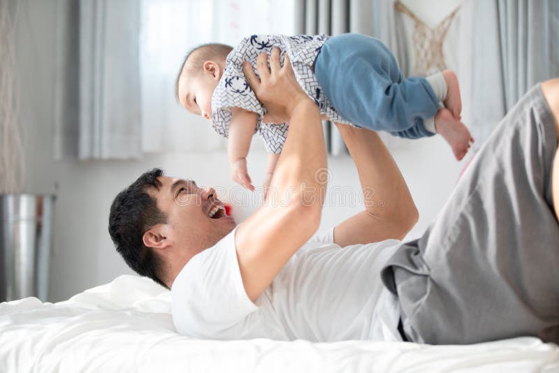 Gelukkige Aziatische familievader met babyzoon het spelen op bed met smil royalty-vrije stock afbeelding Gelukkige Aziatische familievader met babyzoon het spelen op bed met smil royalty-vrije stock afbeelding