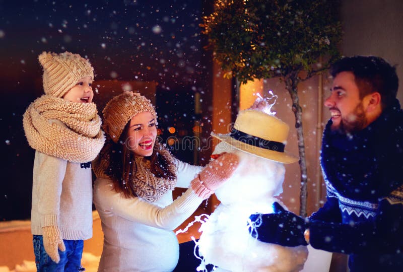 Gelukkige familie die sneeuwman in avondlicht maken onder de wintersneeuw royalty-vrije stock fotografie Gelukkige familie die sneeuwman in avondlicht maken onder de wintersneeuw royalty-vrije stock fotografie