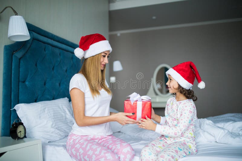 Gelukkige familiemoeder en kinddochter die giften in bed op Kerstmisochtend geven stock foto Gelukkige familiemoeder en kinddochter die giften in bed op Kerstmisochtend geven stock foto