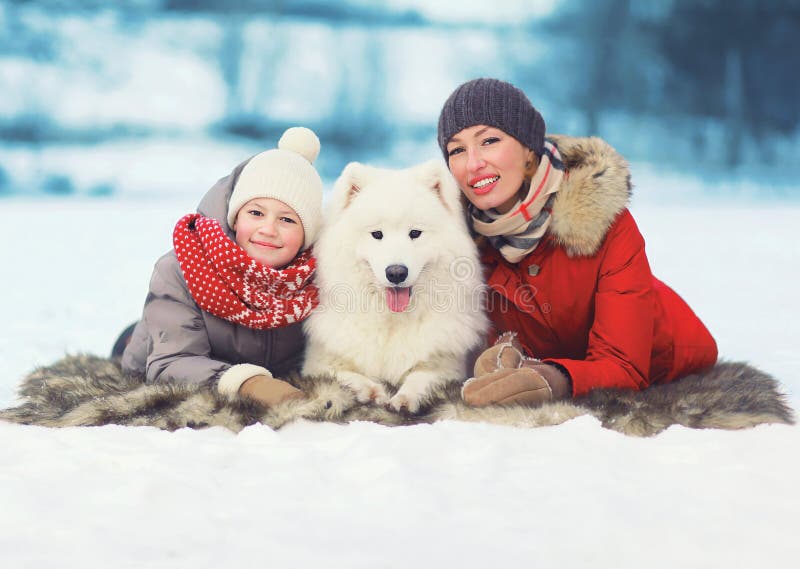 Christmas, winter and people concept - happy smiling family, mother and son walking with white Samoyed dog in winter day. Christmas, winter and people concept - happy smiling family, mother and son walking with white Samoyed dog in winter day