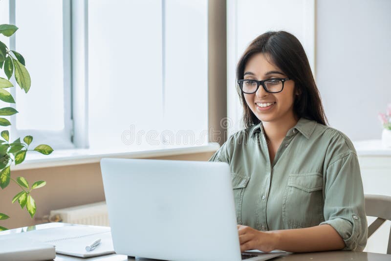 Gelukkige indiase jonge vrouw die een laptop gebruikt voor een werkstudie in thuiskantoor.