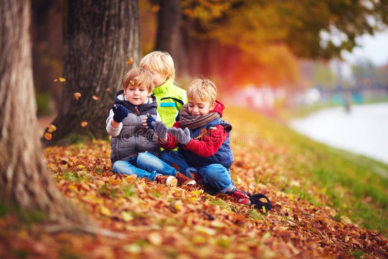 Gelukkige jonge geitjes, vrienden die pret onder gevallen bladeren in de herfstpark hebben stock foto Gelukkige jonge geitjes, vrienden die pret onder gevallen bladeren in de herfstpark hebben stock foto