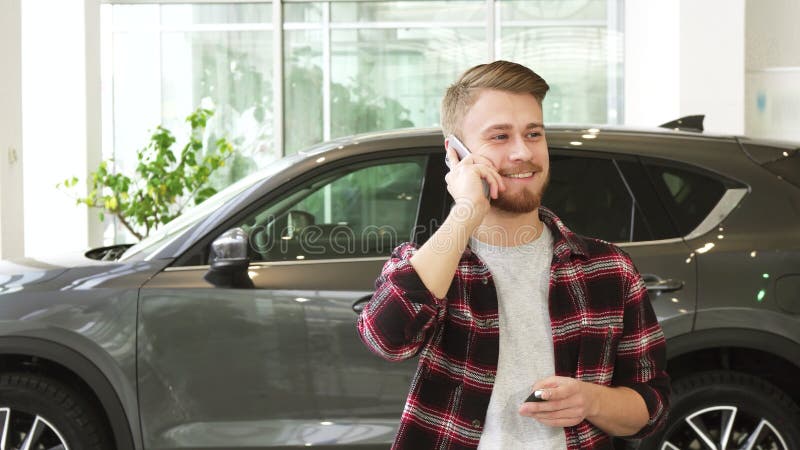 Gelukkige jonge mens die op de telefoon na het kopen van een nieuwe auto bij dealrrship spreken