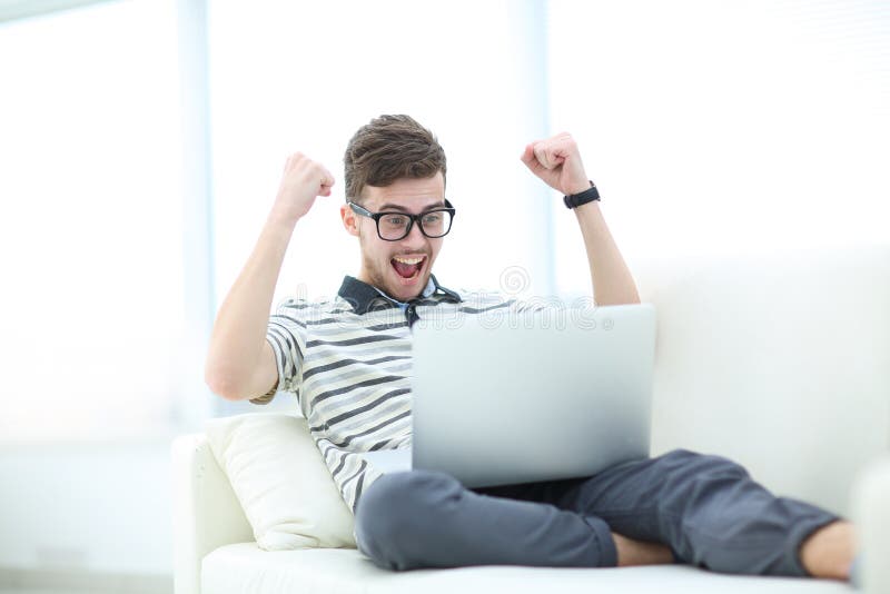 Gelukkige jonge mens die zijn laptop in heldere woonkamer met behulp van stock foto Gelukkige jonge mens die zijn laptop in heldere woonkamer met behulp van stock foto