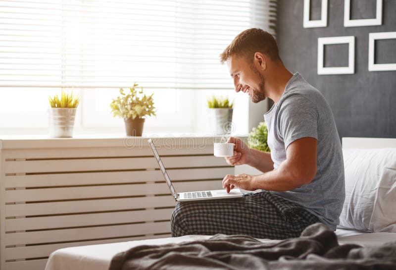 Gelukkige jonge mens met laptop en kop van koffie in bed royalty-vrije stock afbeeldingen Gelukkige jonge mens met laptop en kop van koffie in bed royalty-vrije stock afbeeldingen