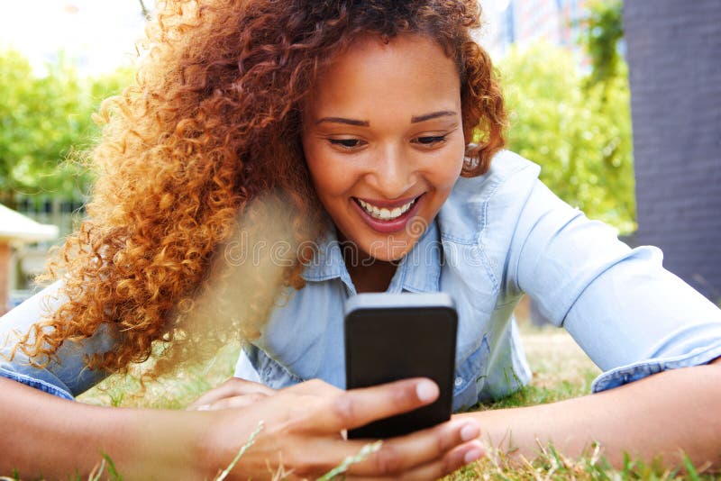 Gelukkige jonge vrouw die in gras liggen en mobiele telefoon bekijken stock foto Gelukkige jonge vrouw die in gras liggen en mobiele telefoon bekijken stock foto