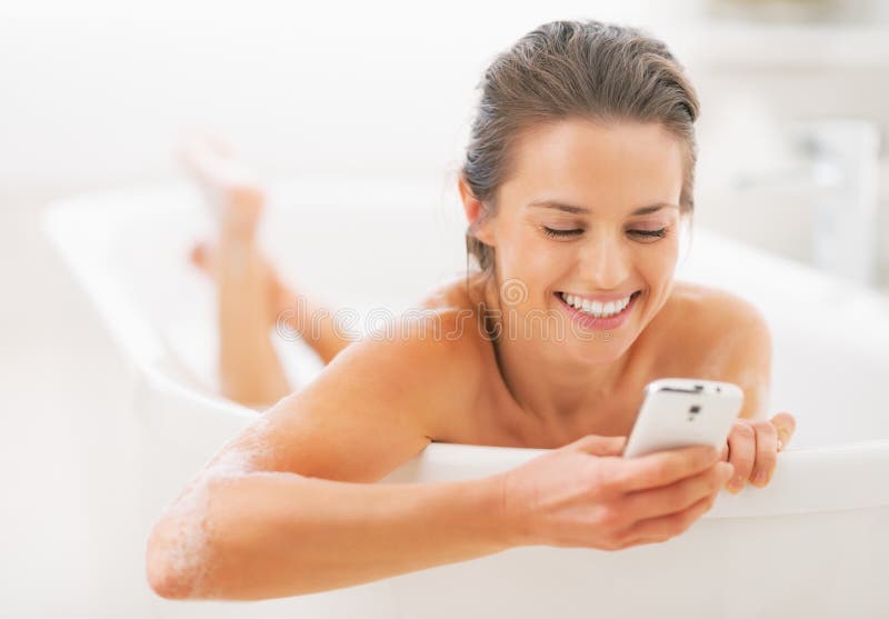 Gelukkige jonge vrouw die sms in badkuip schrijven royalty-vrije stock foto Gelukkige jonge vrouw die sms in badkuip schrijven royalty-vrije stock foto