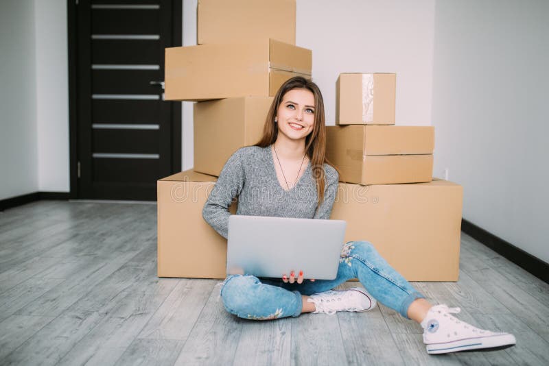 Gelukkige jonge vrouw die zich aan nieuwe huiszitting op de vloer en gebruikslaptop dichtbij dozen bewegen royalty-vrije stock afbeelding Gelukkige jonge vrouw die zich aan nieuwe huiszitting op de vloer en gebruikslaptop dichtbij dozen bewegen royalty-vrije stock afbeelding