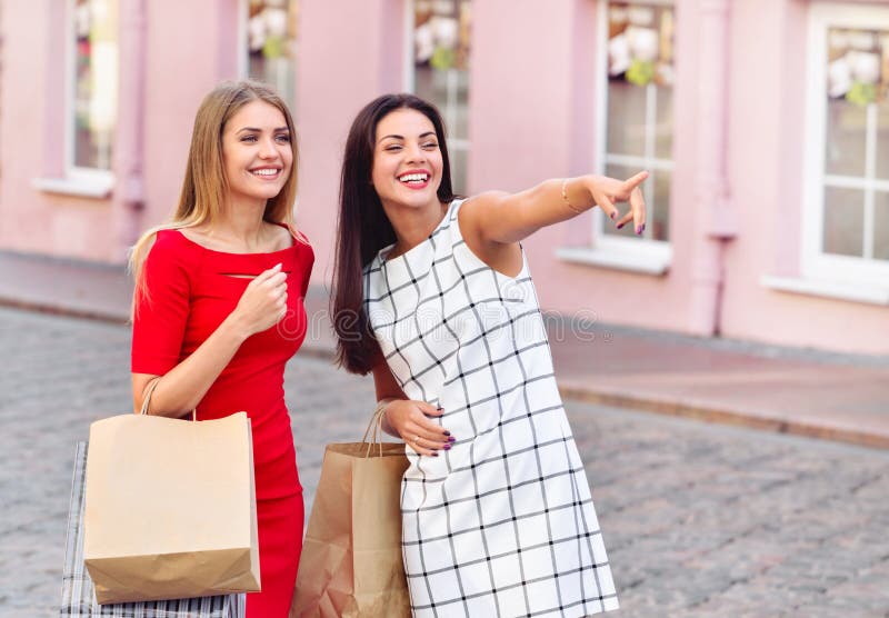 Gelukkige jonge vrouwen die met het winkelen zakken vinger ergens richten stock foto Gelukkige jonge vrouwen die met het winkelen zakken vinger ergens richten stock foto