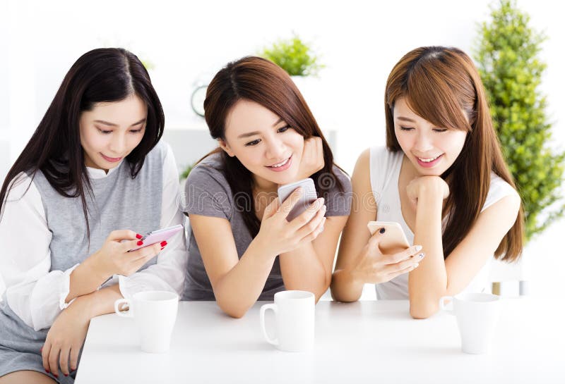 Gelukkige jonge vrouwen die op slimme telefoon in woonkamer letten royalty-vrije stock foto Gelukkige jonge vrouwen die op slimme telefoon in woonkamer letten royalty-vrije stock foto