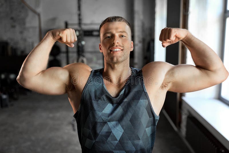 Gelukkige jongeman die zijn biceps in de gym laat zien