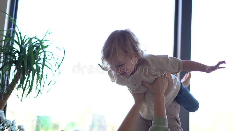 Gelukkige jongeman ligt op comfortabel bed met lachen heerlijke peuterzoon die binnenshuis kietelt. glimlachen