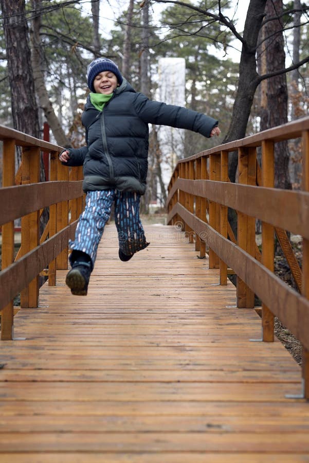 Gelukkige jongen die en op een houten brug in het bos springen lopen royalty-vrije stock afbeeldingen Gelukkige jongen die en op een houten brug in het bos springen lopen royalty-vrije stock afbeeldingen