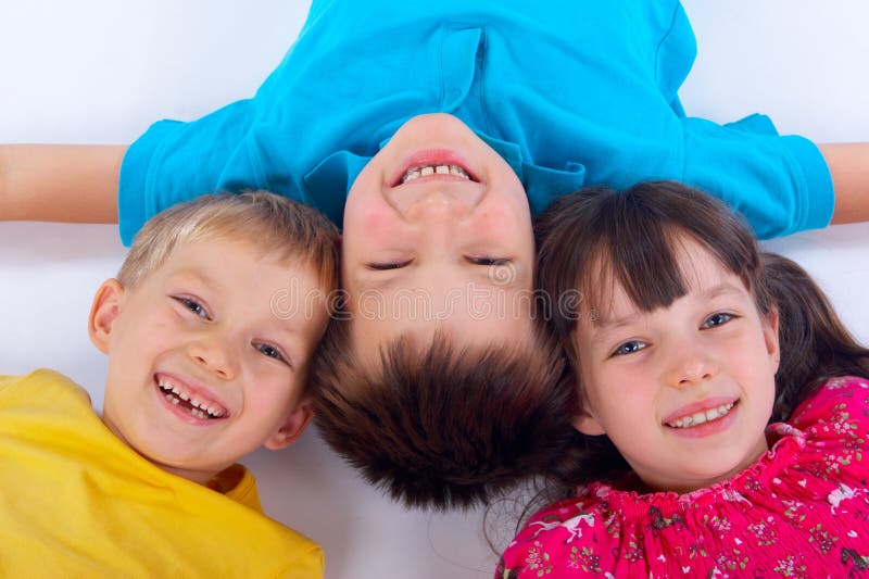 Three happy children in bright colored shirts laying on a white background with happy expressions on their faces. Three happy children in bright colored shirts laying on a white background with happy expressions on their faces.