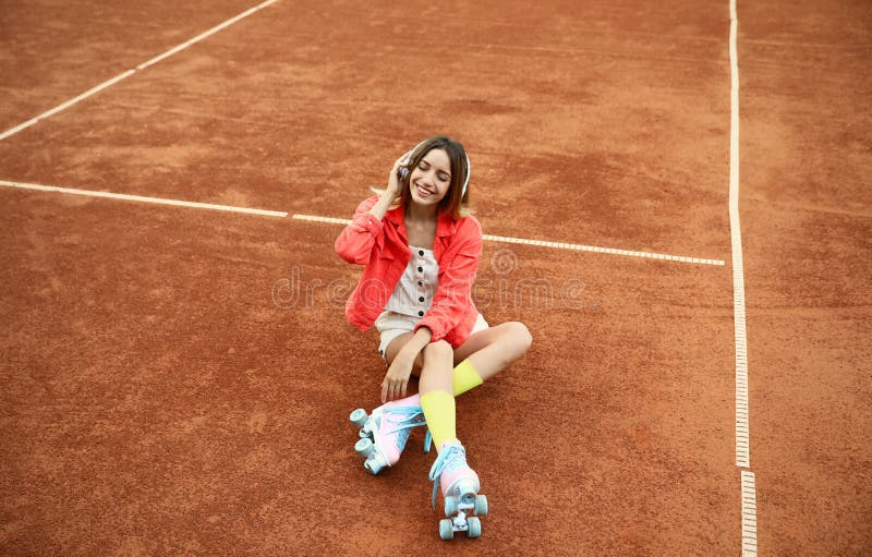 Gelukkige modieuze jonge vrouw met het uitstekende rolschaatsen en hoofdtelefoons zitten stock foto Gelukkige modieuze jonge vrouw met het uitstekende rolschaatsen en hoofdtelefoons zitten stock foto
