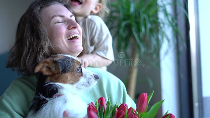 Gelukkige moeder op moederdag houdt een hond en een bouquet tulpen in haar handen terwijl haar zoon haar knuffelt