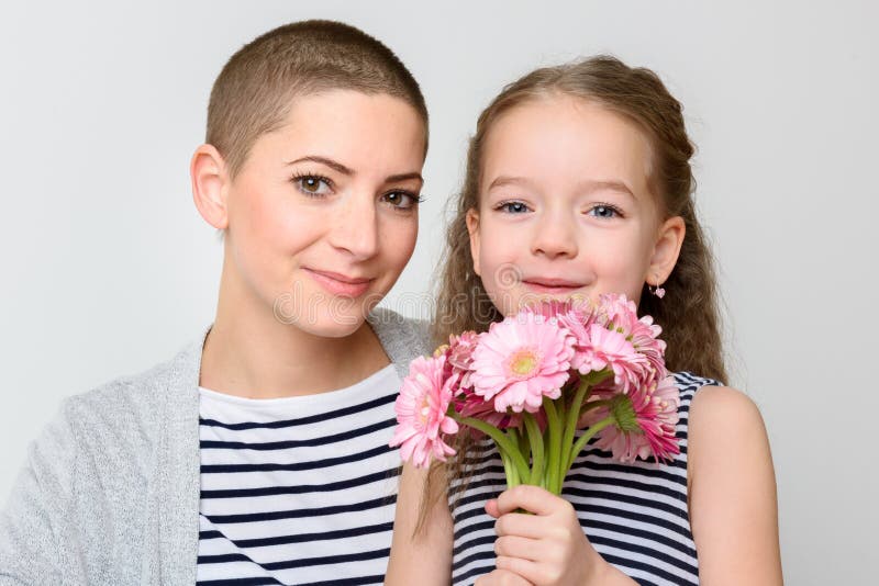 Happy Mother`s Day, Women`s day or Birthday background. Cute little girl giving mom, cancer survivor, bouquet of pink gerbera daisies. Mother and daughter smiling and looking at camera. Happy Mother`s Day, Women`s day or Birthday background. Cute little girl giving mom, cancer survivor, bouquet of pink gerbera daisies. Mother and daughter smiling and looking at camera.