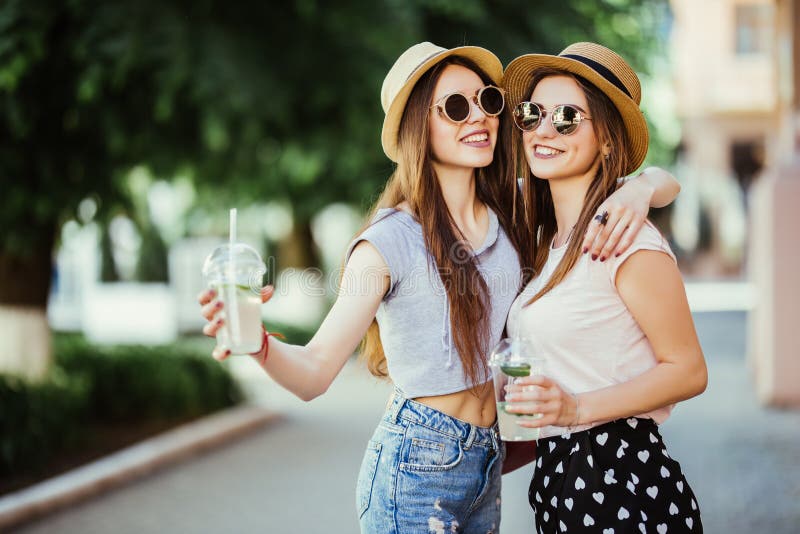 Gelukkige positieve ogenblikken van twee modieuze meisjes die met cocktails op straat in stad koesteren Grappige blije attarctive royalty-vrije stock foto Gelukkige positieve ogenblikken van twee modieuze meisjes die met cocktails op straat in stad koesteren Grappige blije attarctive royalty-vrije stock foto
