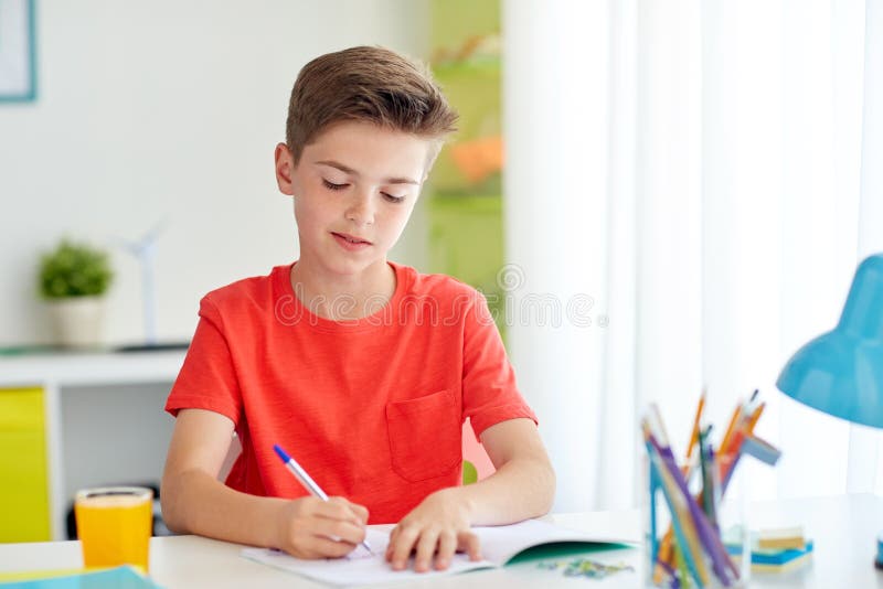 Gelukkige studentenjongen die aan notitieboekje thuis schrijven royalty-vrije stock fotografie Gelukkige studentenjongen die aan notitieboekje thuis schrijven royalty-vrije stock fotografie