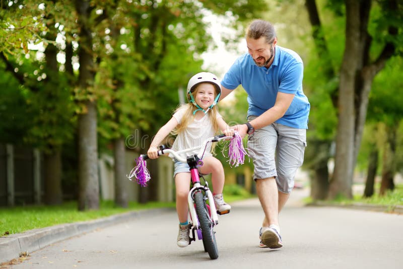 Gelukkige vader die zijn kleine dochter onderwijzen om een fiets te berijden Kind die een fiets leren te berijden