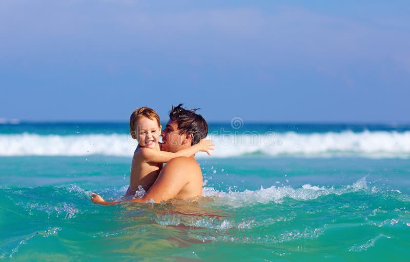 Gelukkige vader en zoon die pret in watergolven hebben royalty-vrije stock foto Gelukkige vader en zoon die pret in watergolven hebben royalty-vrije stock foto