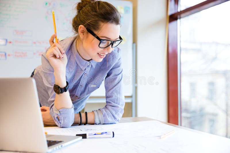 Gelukkige vrouw die met blauwdruk dichtbij het venster in bureau werken stock foto's Gelukkige vrouw die met blauwdruk dichtbij het venster in bureau werken stock foto's