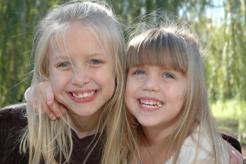 Two beautiful little blond sisters hug each other and laugh. Sisters having a fun time together at the park. Two beautiful little blond sisters hug each other and laugh. Sisters having a fun time together at the park.