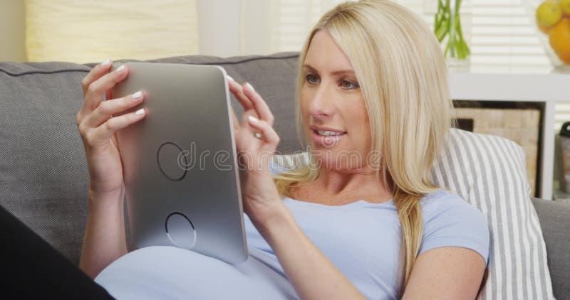 Gelukkige zwangere vrouw die op laag liggen die tablet gebruiken stock foto Gelukkige zwangere vrouw die op laag liggen die tablet gebruiken stock foto