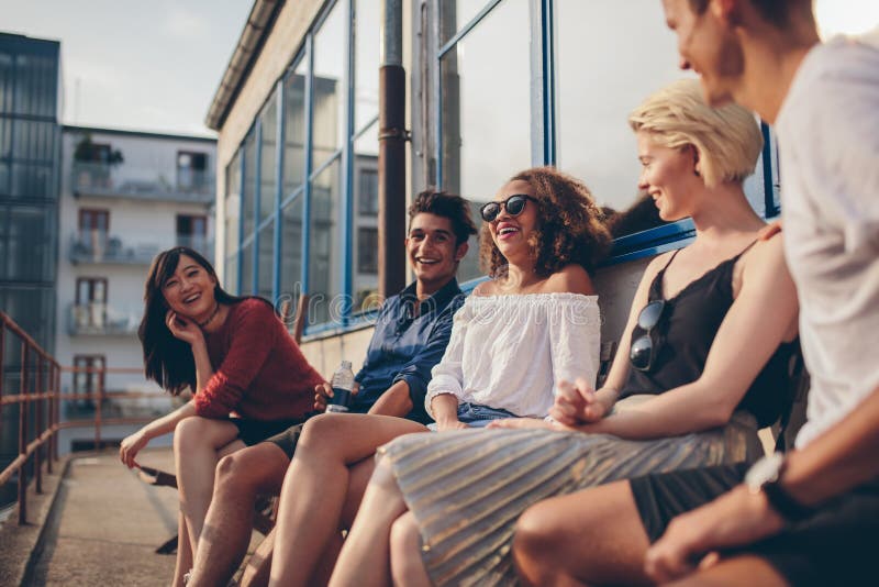 Gemischtrassige Gruppe Freunde, die im Balkon und im Lächeln sitzen stockbilder Gemischtrassige Gruppe Freunde, die im Balkon und im Lächeln sitzen stockbilder