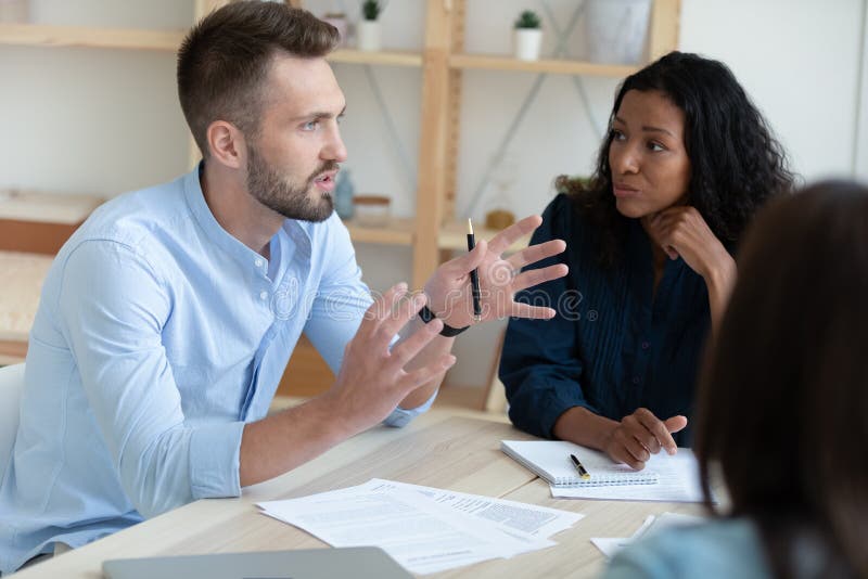 Close up of motivated diverse employees talk in group discuss company financial paperwork in office together. Multiethnic colleagues coworkers brainstorm consider documents at team briefing. Close up of motivated diverse employees talk in group discuss company financial paperwork in office together. Multiethnic colleagues coworkers brainstorm consider documents at team briefing.