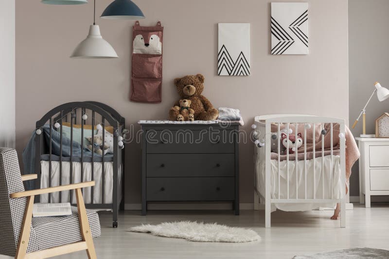 Cozy bedroom interior for twins with white and gray baby beds, a chest of drawers and a fluffy rug. Cozy bedroom interior for twins with white and gray baby beds, a chest of drawers and a fluffy rug