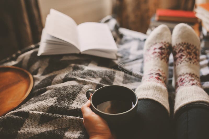 Gemütlicher Wintertag zu Hause mit Schale heißem Tee, Buch und warmen Socken