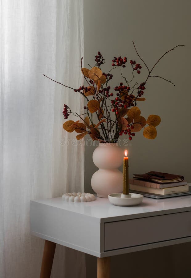 Gemütliches Herbstleben ein Strauß von Herbstblättern in einer Vase Bücher eine brennende Kerze auf einem weißen Tisch stockfotografie