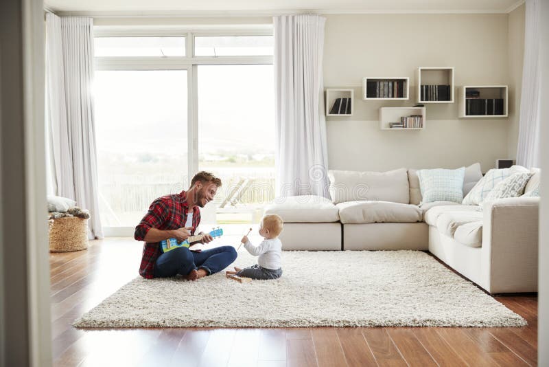 Gene o jogo da uquelele com o filho novo em sua sala de estar fotografia de stock Gene o jogo da uquelele com o filho novo em sua sala de estar fotografia de stock