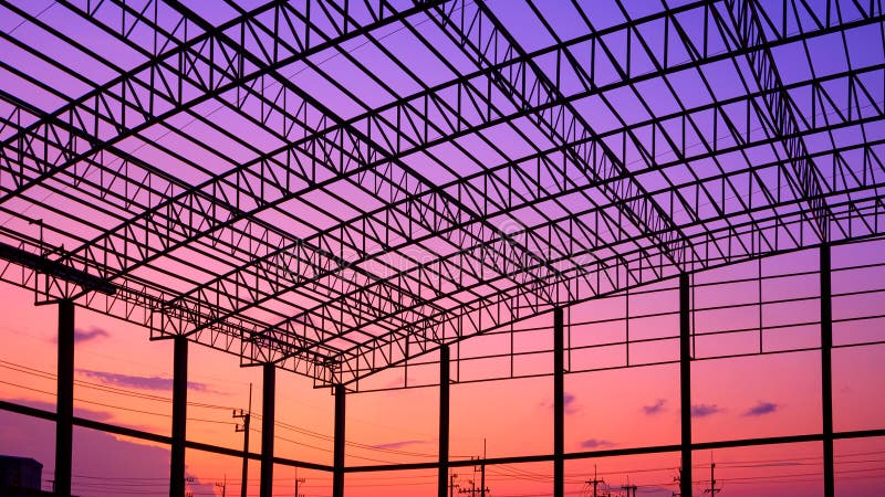 Silhouette of incomplete factory building structure with curve metal roof beam against colorful twilight sky