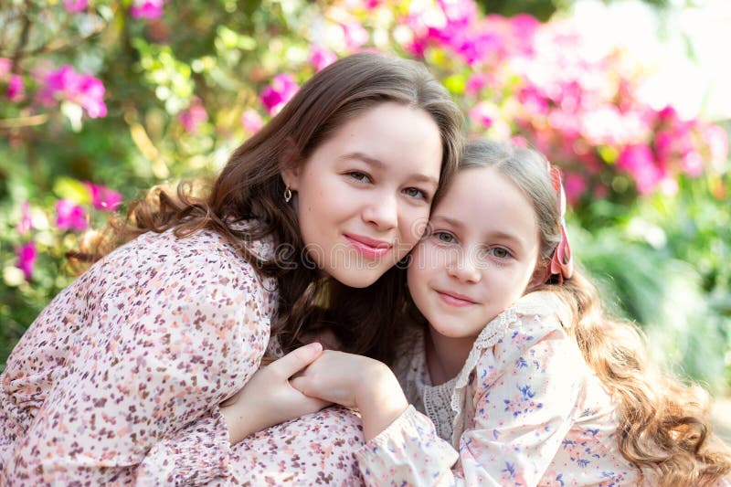 Closeup portrait smiling teen girl sister embracing little girl in greenhouse among flowers, feeling love and connection