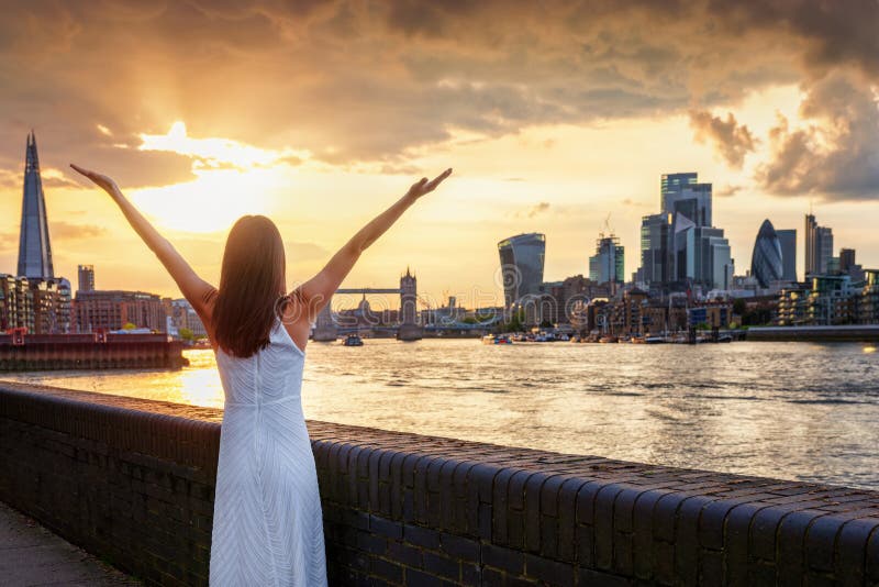A tourist woman enjoys the beautiful sunset view of the city skyline of London