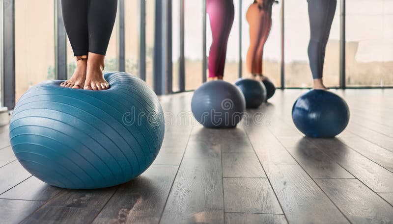 Barefoot individuals in exercise leggings stand in a row on a wooden gym floor. Black and blue medicine balls are aligned in front of them. The setting features large windows, allowing natural light to illuminate the space. The scene suggests a fitness class or group workout session. Aerobics pilates women feet with yoga balls in a row on fitness class. Al Generated. Pilates leg illustrations